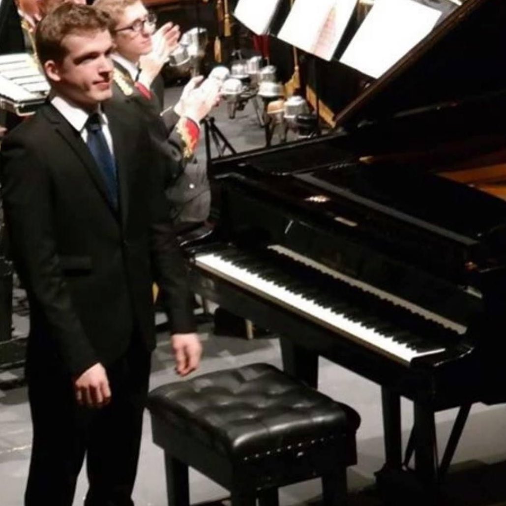 Image of a young man stood next to a piano