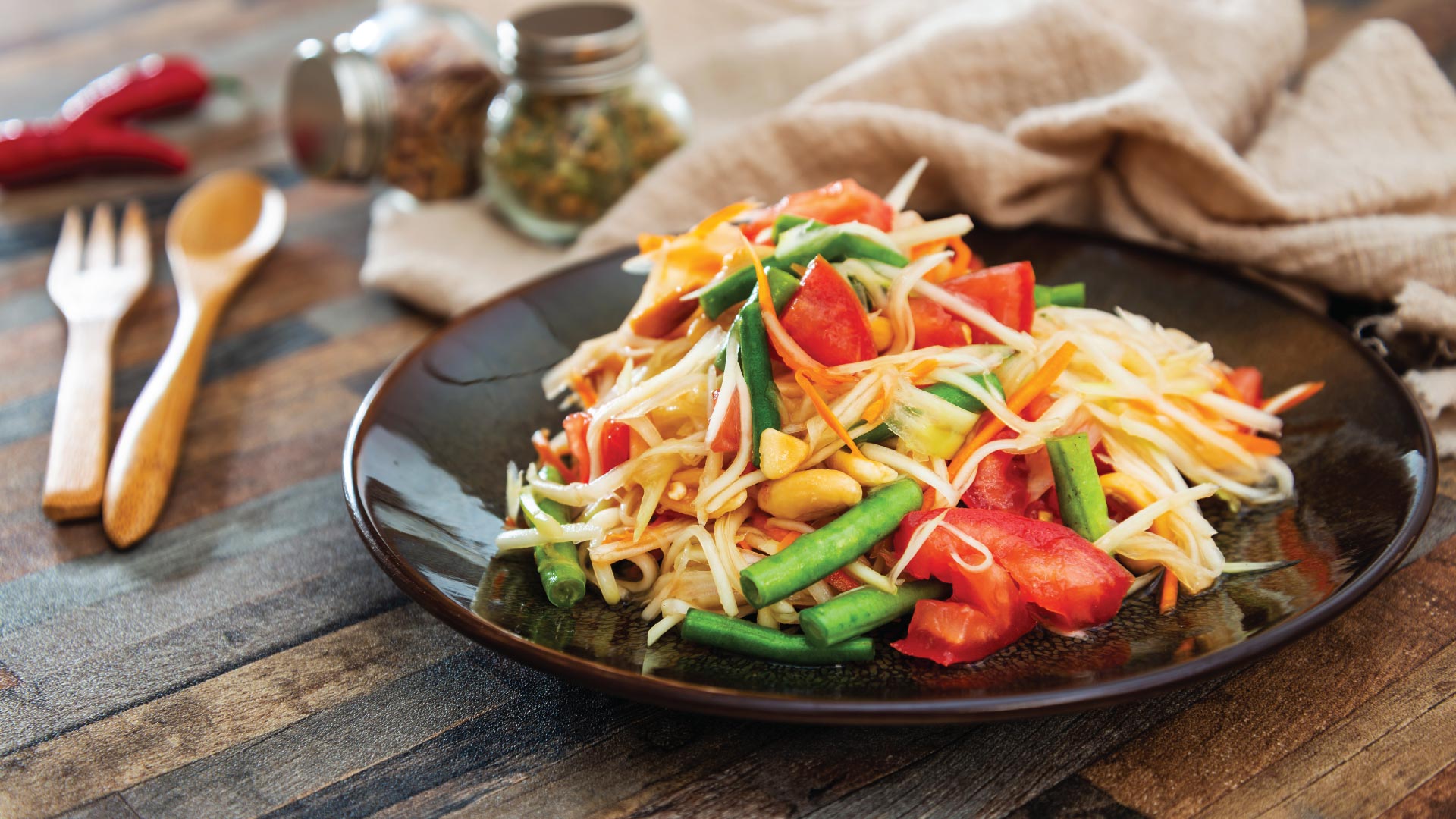 Traditional Thai food papaya salad prepared with fine slices of papaya, tomatoes, green beans and peanuts.