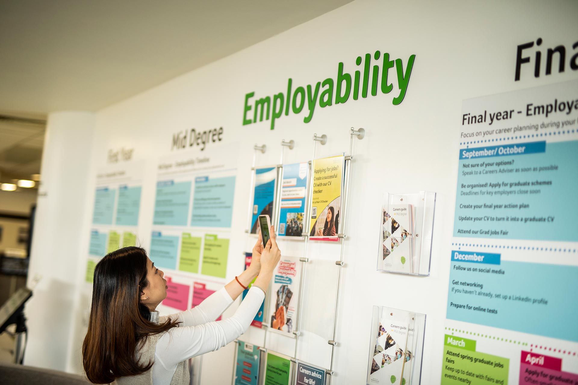 A student taking a photo of information on a Careers and Employability information wall.