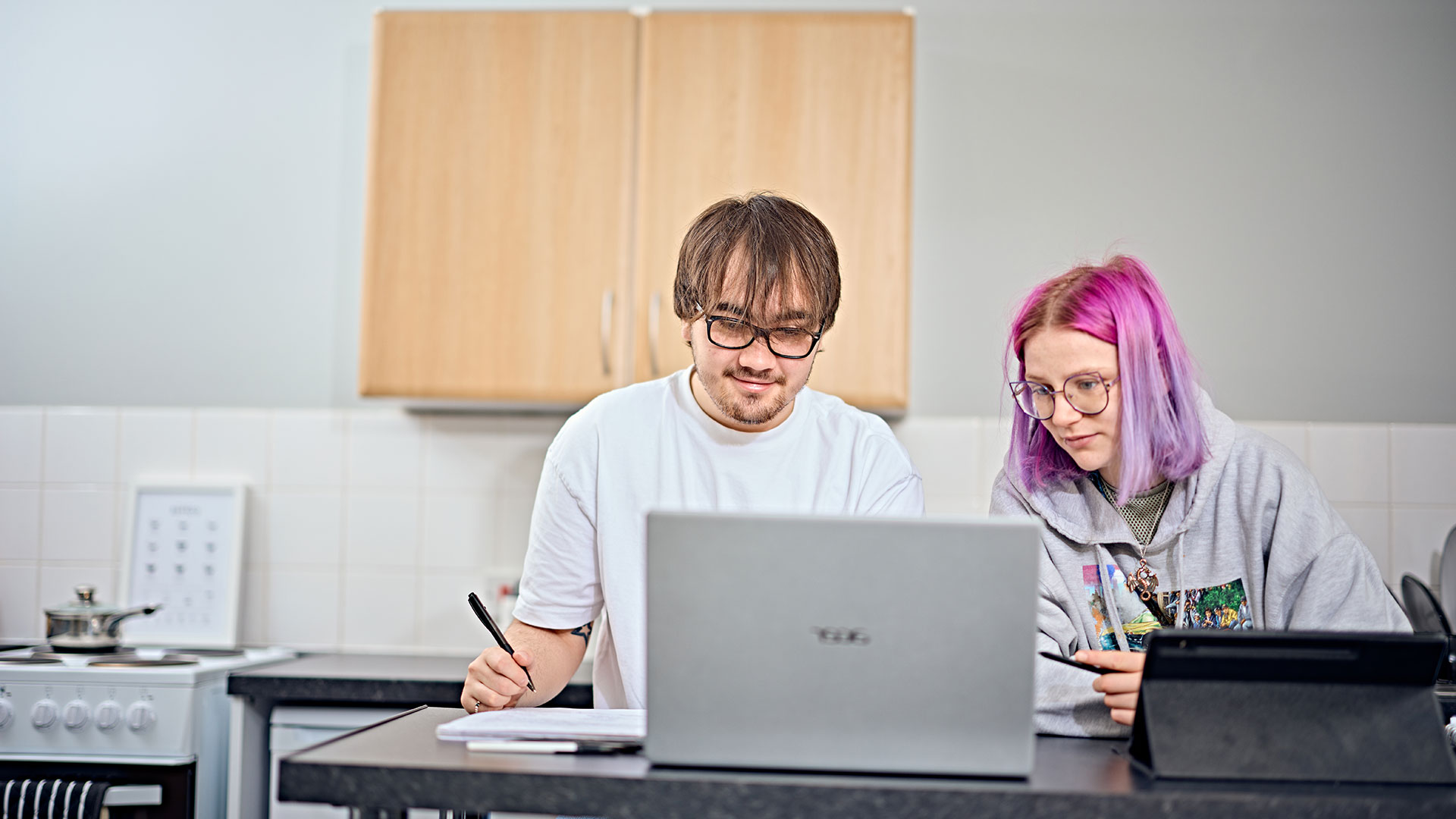 Two students sat at a breakfast bar, looking at a laptop.