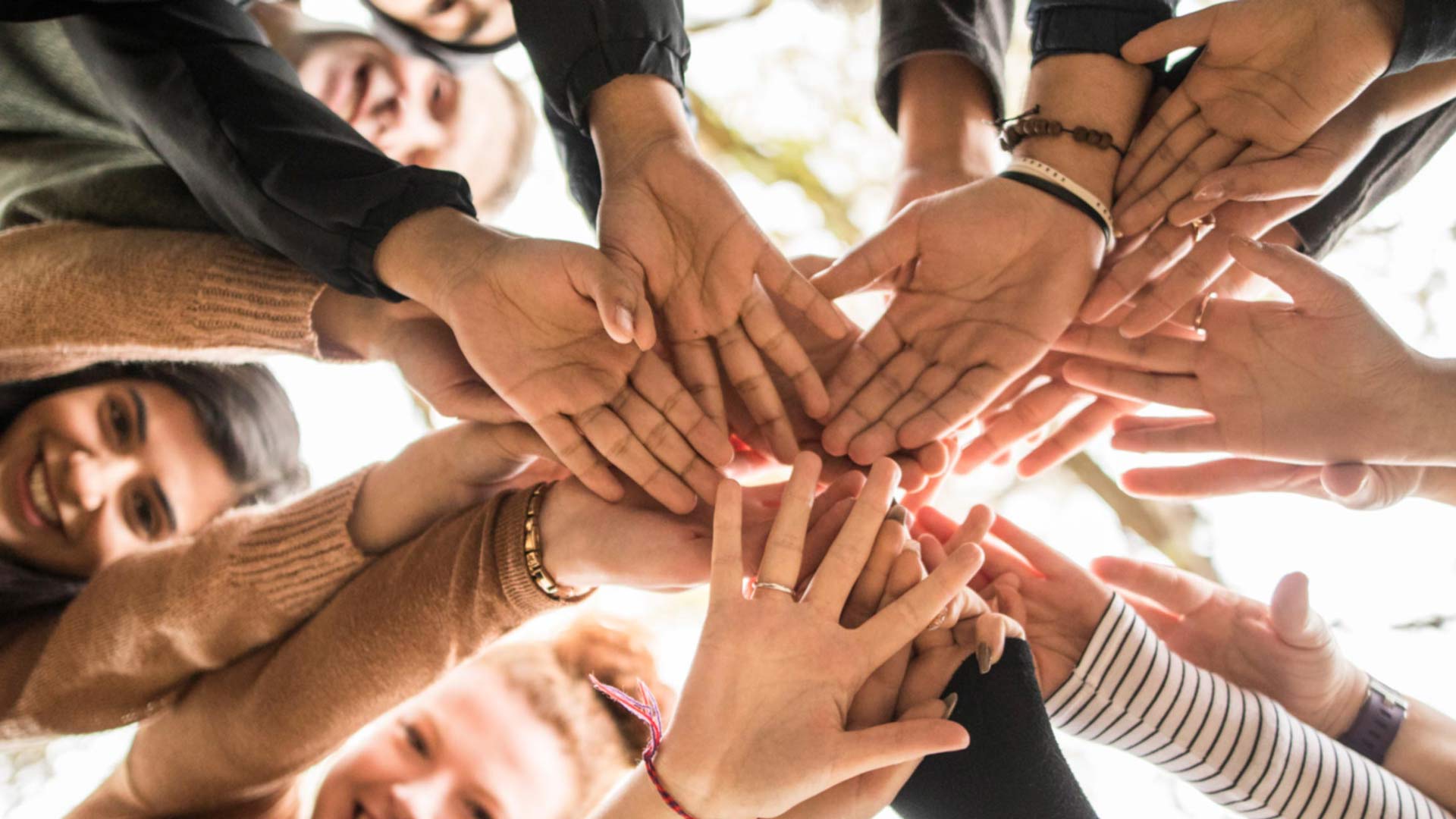 11 students stood in a circle with their hands in the centre looking down to the camera.