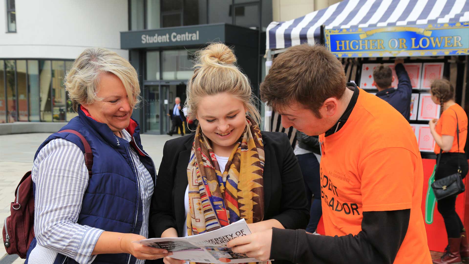 A Student Ambassador helps a parent and potential student look through the open day booklet. 